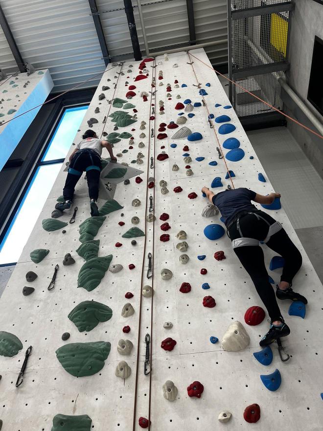 Deux participants de la section en pleine ascension côte à côte sur un mur d'escalade coloré.