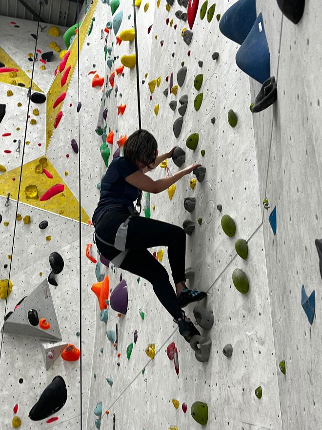 Une jeune femme grimpe un mur de grimpe en toute sécurité à l'aide d'un système d'auto-assureur.